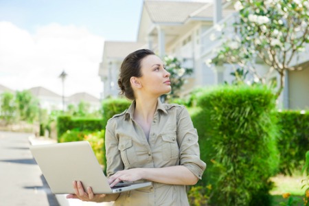 Female real estate agent with laptop outside homes