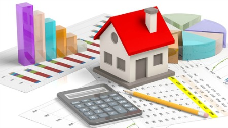 real estate market concept with small house sitting on papers with calculator and pencil