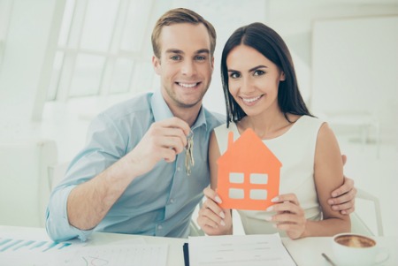 smiling man and woman holding keys and house cut out